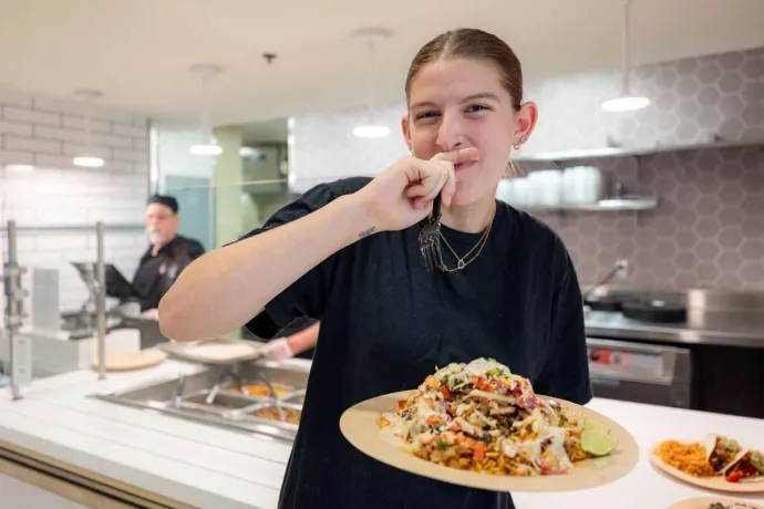 A young woman is holding a plate of food and smiling while about to take a bite at Taco Santo.