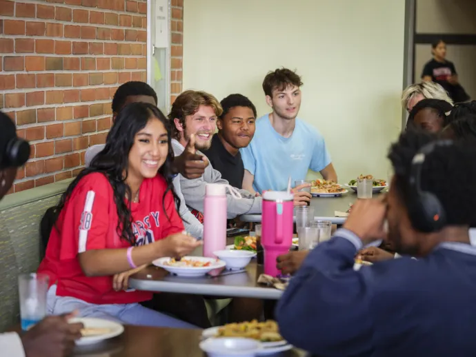 Students enjoying meal at long table together in dining hall