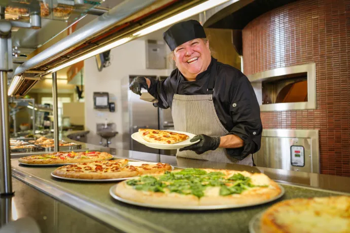 Employee smiling while serving a slice of pizza behind counter